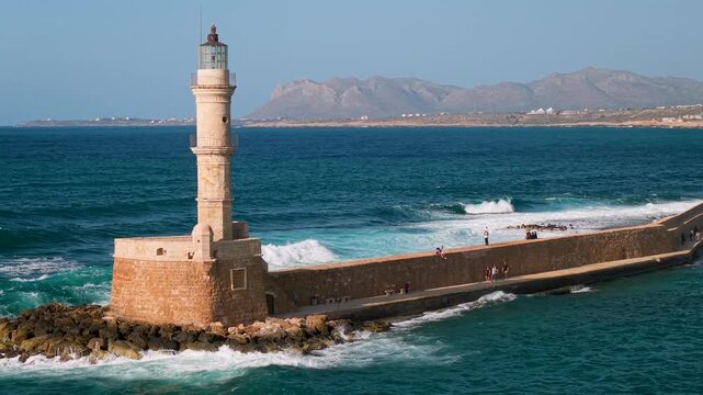 Greece Crete Chania 4K Drone Video of Venetian Lighthouse with Crashing Waves and Greek Flag Flying on Foreground Cinematic Side Tracking Aerial Travel Shot