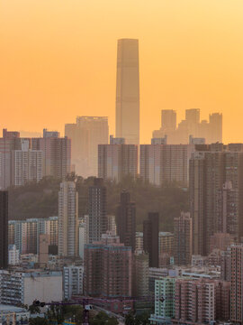 The towering International Commerce Centre rises above the dense residential blocks of Hong Kong during a hazy golden sunset.