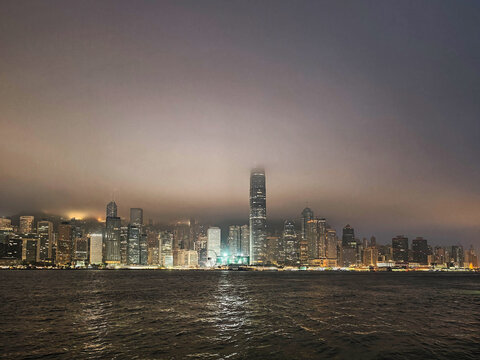The illuminated skyline of Hong Kong stands majestic as low clouds and fog shroud the tops of skyscrapers over Victoria Harbour at night.