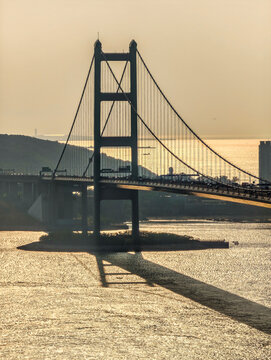 The Tsing Ma Bridge spans the water at sunset, connecting to a complex highway interchange in Hong Kong.