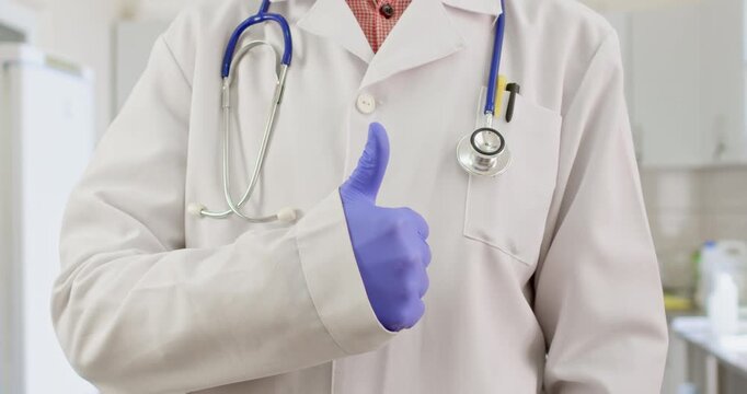 A doctor in a white coat and a stethoscope on his neck shows a thumb up.
