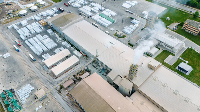 Aerial view of a large industrial facility with warehouses, smoking chimneys, and stacked cargo pallets in Sabac, Vojvodina, Serbia.