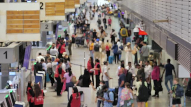 Lengthwise perspective of modern airport check-in concourse, captured with intentional soft focus to maintain anonymity. Abstract movement of passengers strolling around airport