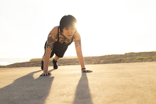 Young tattooed woman exercising push ups outdoors