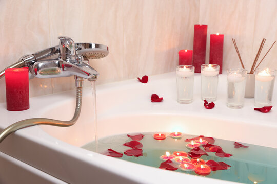 Romantic atmosphere. Bathtub with burning candles, air reed freshener and petals in bathroom, closeup
