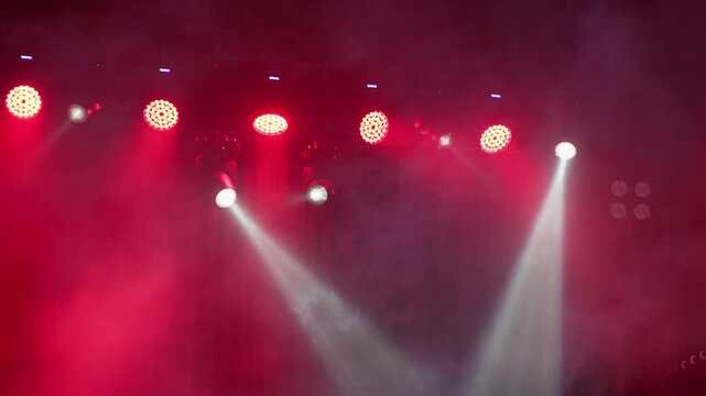 Abstract view of red stage spotlights glowing through haze and smoke on an empty concert stage, creating a dramatic atmospheric backdrop