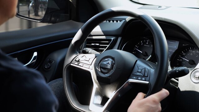 Male arms holds steering wheel while driving a motor car at city. Young man operating the automobile at urban road. Driver moving in his auto on route. Slow motion