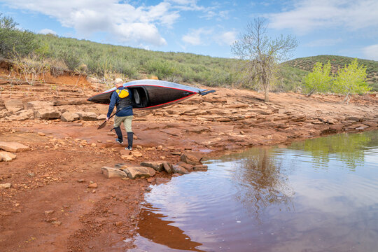 senior paddler is launching his decked touring canoe on shore of Horsetooth Reservoir - early spring scenery of Colorado foothills