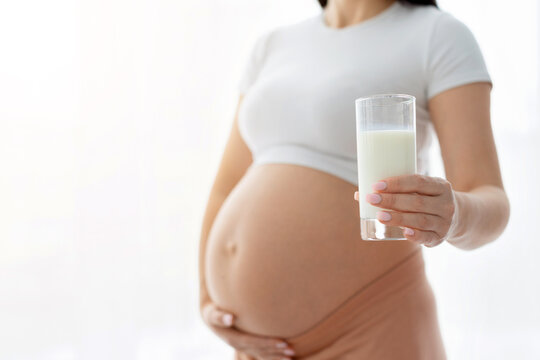Closeup of pregnant woman holding glass of milk in hand, highlighting nutrition, calcium intake and prenatal health concept in clean bright environment