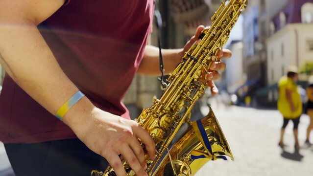 Male fingers of musician play the saxophone on summer day. Natural light reflects off metal surface, highlighting movement and rhythm. Scene captures live urban music and atmosphere street performance