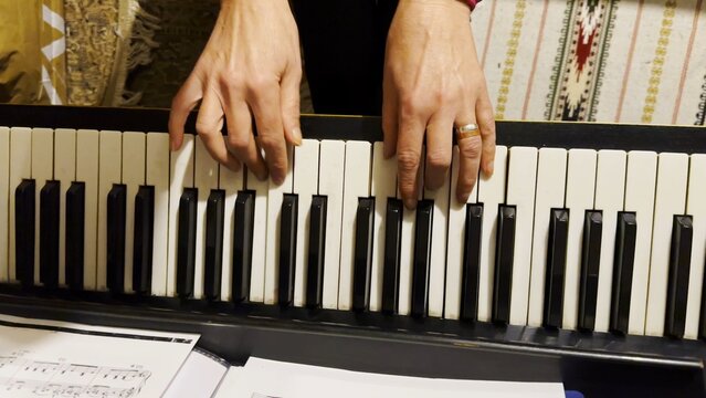 Top view of adult female hands playing gentle piece of classical music on black piano. Scene captures the movement, rhythm and elegance of performance, highlighting beauty of live instrumental play