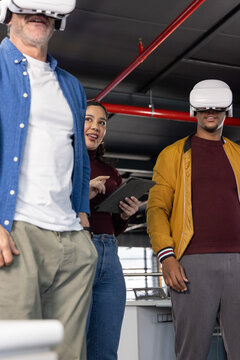 Diverse coworkers wearing white VR headsets following tablet guidance in office with red pipes