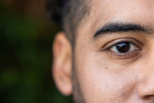 Man facing right, filling frame, revealing right eye and stubble with green bokeh background