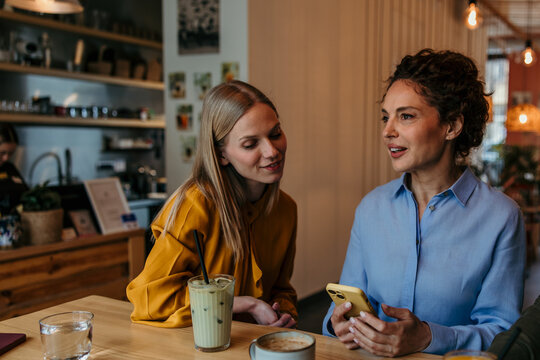 Women friends using smartphone and talking in cafe