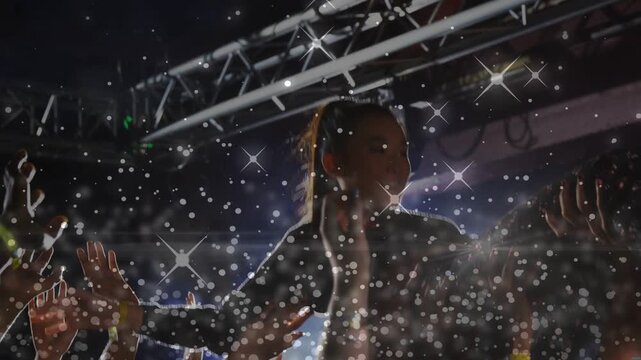 Female performer being crowd-lifted in concert, singing into mic while sparkles highlighting hands