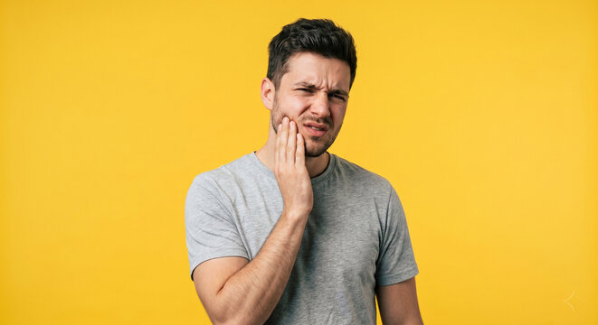 Young man with severe toothache touching cheek on yellow background, dental pain and oral health problem
