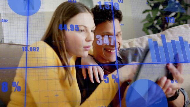 Woman leaning and man adjusting tablet, tapping to activate blue charts while reviewing finances