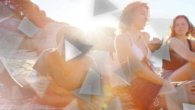 Five friends chatting on striped mat, sun flaring causing triangles obscuring relaxed group, travel