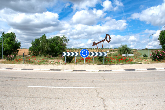 Rotonda en carretera rural con se&ntilde;ales de tr&aacute;fico y escultura met&aacute;lica bajo cielo nublado.