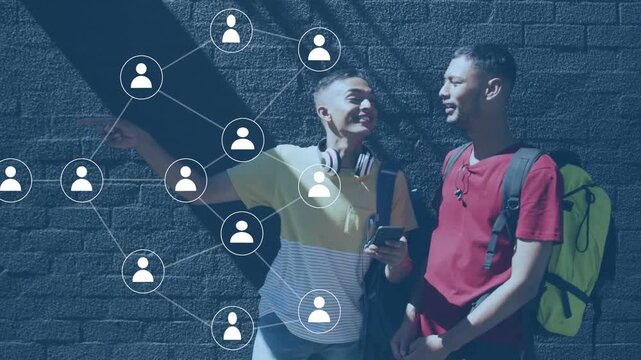 Two men leaning on brick wall, left man pointing and tapping phone, creating social network overlay