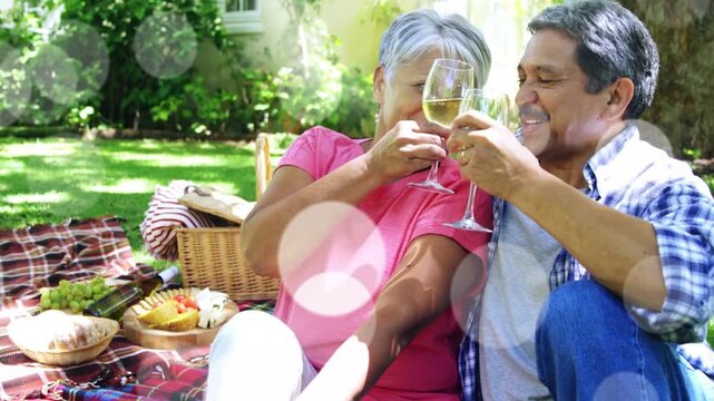 Senior couple raising glasses smelling sipping leaning and smiling as bokeh floating for lifestyle