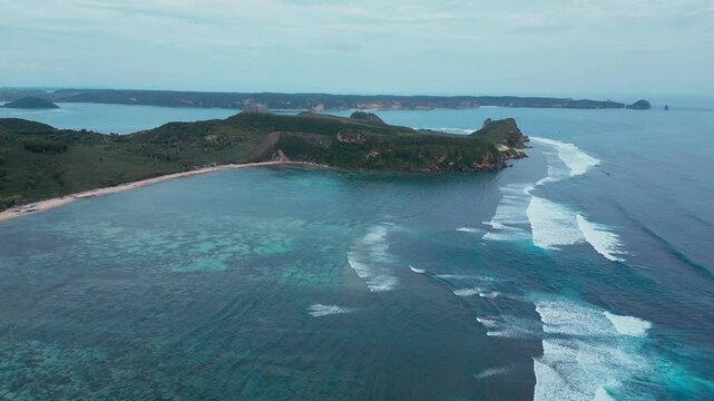 Aerial Green Island Cape With Curved Beaches, Rolling Hills And Farmland Pockets, Long Reef Line Shaping Waves, Secluded Bays, Turquoise Shallow Water Meeting Deep Ocean, Katil beach,Lombok,Indonesia