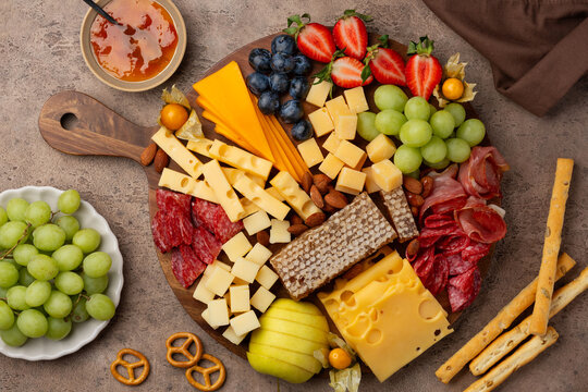 A cheese platter with salami, ham, berries, grapes, apple, physalis, and honeycomb on a brown background. Various types of cheese. An appetizer for company. Top view.