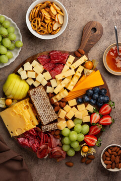 Cheeseboard with berries, nuts, salami, ham, grapes, physalis and honeycomb on a brown background.  Top view. A festive party appetizer