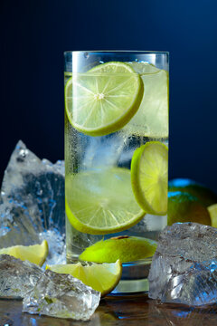 Cold refreshing drink with ice and lime in tall glass with water condensation drops.