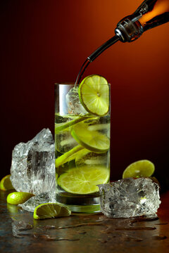 Vodka is poured from a bottle into a glass with ice and lime slices.