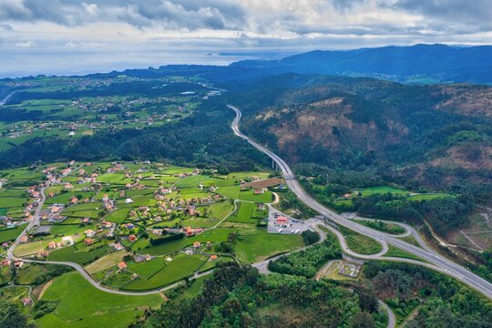 Aerial view of the Autovia del Cantabrico highway winding through lush green hills and rural villages under a cloudy sky Cudillero, Asturias, Spain.
