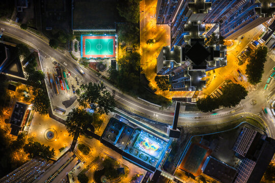 Brightly lit green football pitch next to a busy bus terminus at night in Hong Kong captures the vibrant energy of high density urban living.