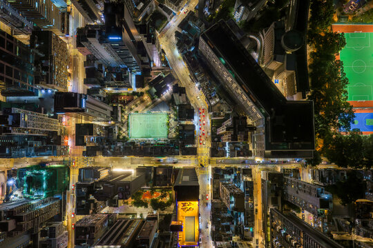 Top down night view of a glowing green sports court nestled among dense urban buildings and busy streets in Hong Kong, Hong Kong.
