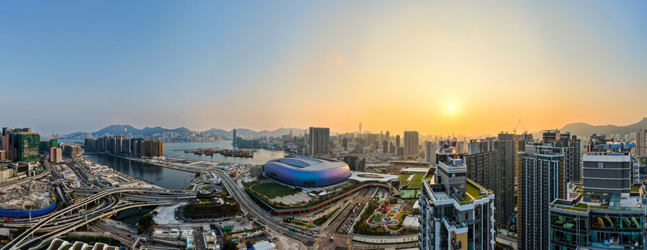 Panoramic sunset view over Kai Tak Sports Park and the dense urban landscape of Hong Kong showcasing modern architectural growth and coastal beauty.