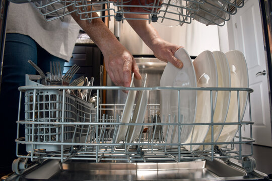 Woman unloading clean dishes from dishwasher seen from inside the appliance. Everyday home chore with point of view perspective, highlighting domestic routine, cleanliness, and modern kitchen living