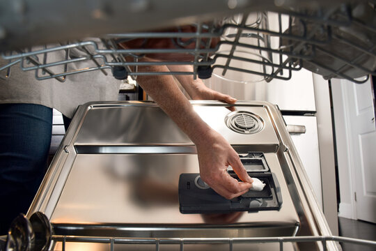 Woman inserting dishwasher detergent pod into appliance compartment, seen from inside the machine. Point of view perspective highlighting modern kitchen routine, cleaning efficiency