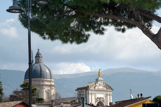 Basilica of Saint Mary of the Angels built in the Mannerist style in 1569 with the gold Virgin Mary statue on the portali. The mount Subasio in the background. Assisi, Perugia, Italy.
