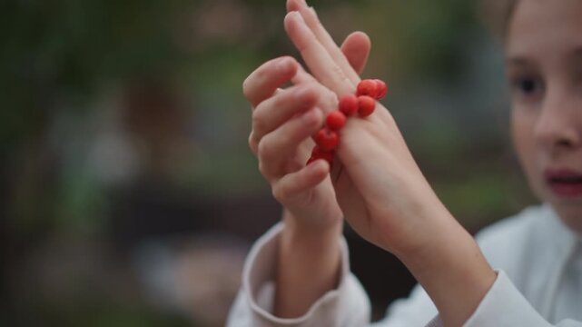 Hands threading red beads on finger, young girl practicing dexterity outdoors closeup, sliding round beads along string and finger playful curiosity, focused expression, shallow depth of field, warm
