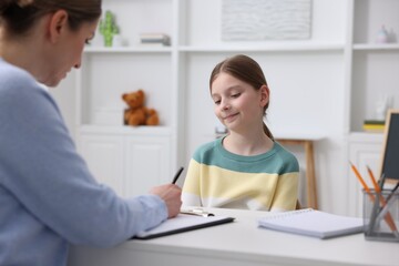 Fototapeta premium Professional child psychologist working with girl at white table indoors