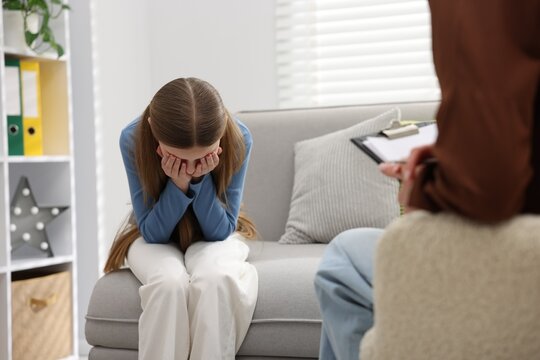 Professional child psychologist working with upset girl on sofa indoors