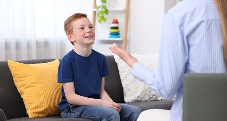 Fototapeta premium Professional child psychologist working with boy on sofa indoors