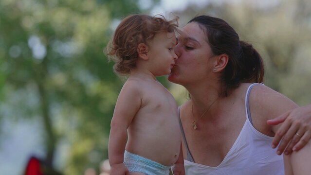Mother kissing toddler on cheek during summer picnic, warm and affectionate outdoor family moment filled with love, tenderness, and emotional bonding