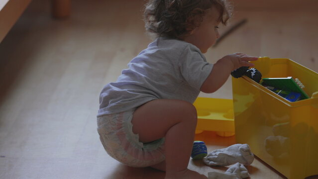 Curly haired toddler crawling on wooden floor at home, playful moment while exploring surroundings and moving towards toys