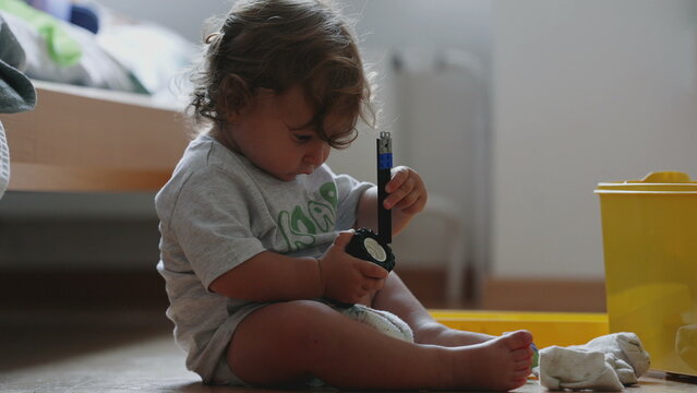 Curly haired toddler sitting on floor playing with toy parts, focused and curious, exploring objects and learning through play at home