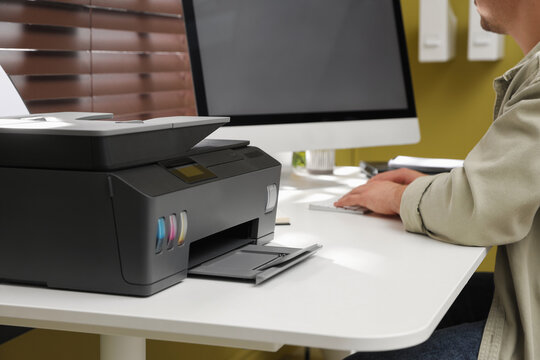 Man working with computer near printer at white desk indoors, closeup