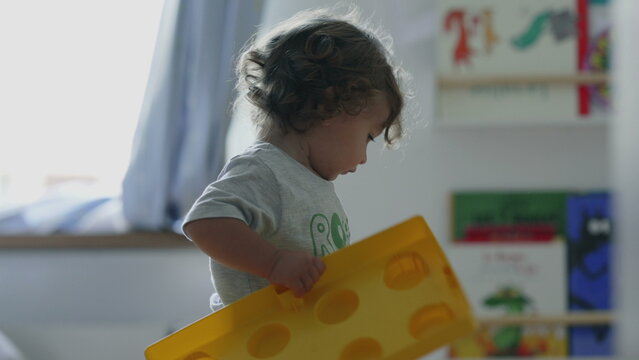 Curly haired toddler standing beside large yellow toy box, playing and exploring, curious and active moment indoors at home