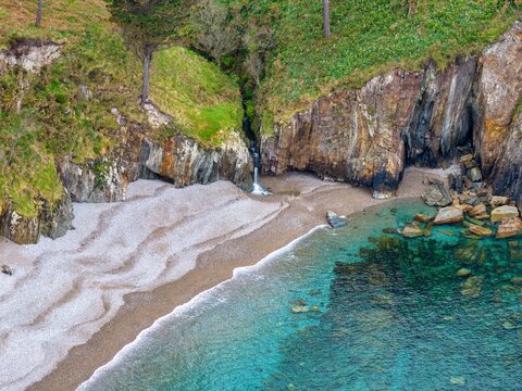 Aerial view of Silence Beach Viewpoint with its dramatic rocky cliffs, a small waterfall, and crystal clear turquoise water in Cudillero, Asturias, Spain.