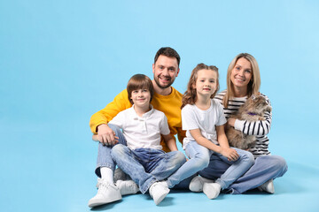 Fototapeta premium Happy family with their cute cat on light blue background, space for text. Adorable pet