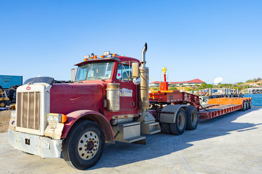 Willemctad, Curacao - 22.03.2026: Red classic Peterbilt semi truck with lowboy trailer parked in a harbor area under a clear blue sky