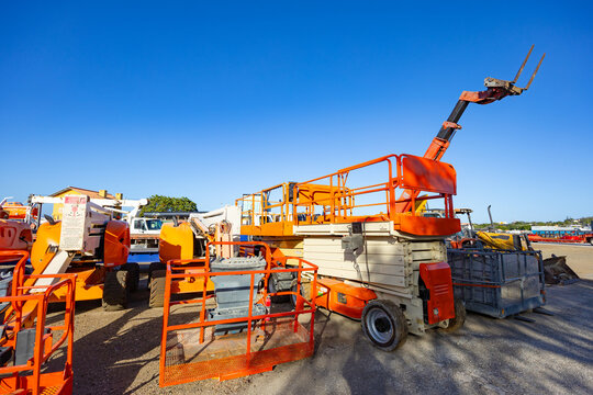 Variety of orange construction machinery including a scissor lift and a telescopic handler with forks under a blue sky